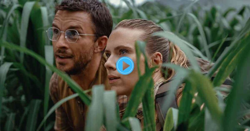 A man with glasses and a beard and a woman with her hair tied back look cautiously into the distance, surrounded by thick, vertical green leaves, suggesting they are hiding in a field or jungle.