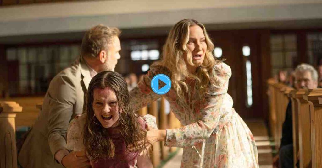 A tense scene from The Exorcist: Believer showing a young girl, covered in blood, being held by two adults in a church aisle as she screams and struggles.