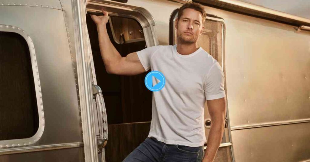 Justin Hartley posing in a casual white t-shirt, leaning on the open door of a vintage-style silver travel trailer.