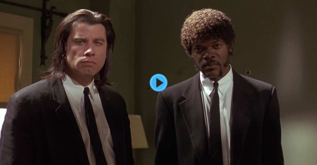 An iconic movie still from Pulp Fiction showing John Travolta with long hair and Samuel L. Jackson with a jheri curl, both wearing black suits and ties, staring straight ahead in a dimly lit room.