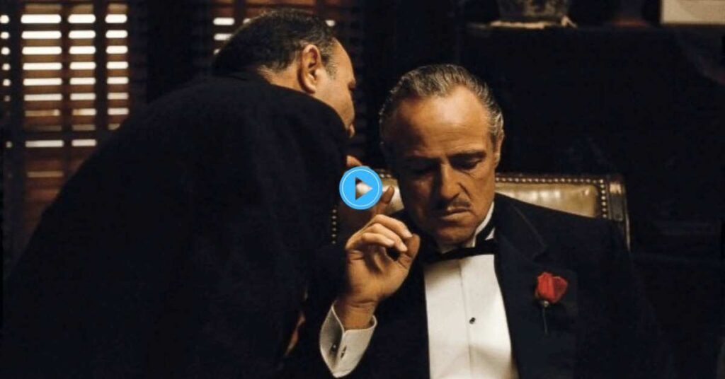 An intensely lit scene from The Godfather featuring a focused Vito Corleone looking down as he is closely advised by a man standing just behind his right shoulder.